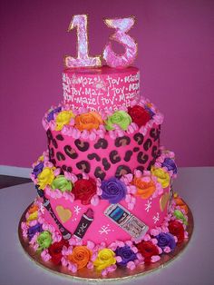 a pink birthday cake decorated with flowers and the number thirteen