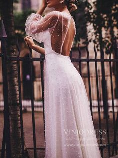 a woman in a white dress leaning on a fence with her back to the camera