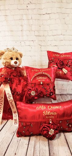 a teddy bear sitting on top of a red bag with some pillows and a ribbon around it