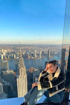 a man sitting on top of a tall building next to a cityscape and looking at the camera