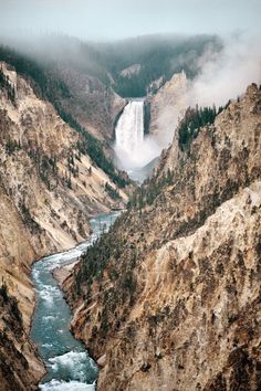 a river flowing through a canyon next to a mountain side covered in fog and mist