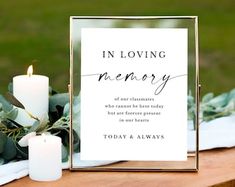 a memorial sign sitting on top of a wooden table next to white candles and greenery