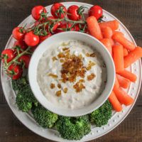 a white plate topped with carrots, broccoli and dip surrounded by cherry tomatoes