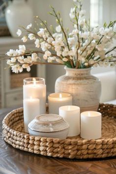 a tray with candles and flowers in it on a table next to a vase filled with white flowers