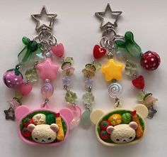 two key chains with charms attached to them on a white surface, one is shaped like a bear and the other has fruit in it's mouth