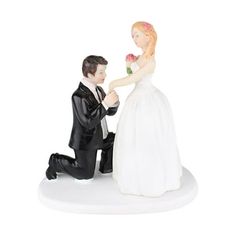 a bride and groom figurine sitting next to each other on a white surface