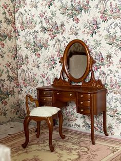 an antique dressing table and chair in front of a floral wallpaper