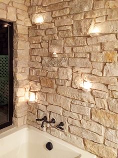 a bath tub sitting next to a stone wall with lights on it's side