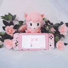 a stuffed animal sitting on top of a pink nintendo wii game console surrounded by flowers