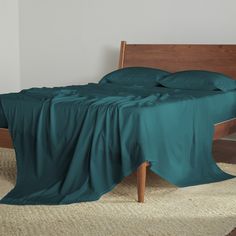 a bed with green sheets and pillows in a white room next to a wooden headboard