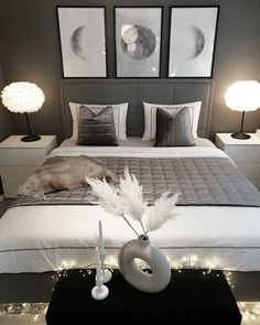 a white bed topped with lots of pillows next to two lamps and pictures on the wall