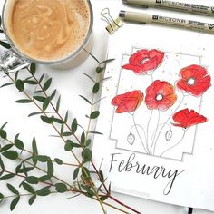 a cup of coffee and some flowers on a white table next to two markers with the word february written in them