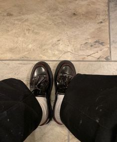 a pair of black shoes sitting on top of a marble floor next to a person's legs