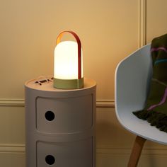 a small table with a lamp on it next to a white chair and green blanket