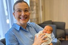 a woman holding a baby in her arms and smiling at the camera while wearing glasses