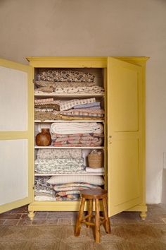 a yellow cabinet filled with lots of folded towels and blankets on top of stools