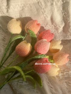 small crocheted flowers sitting on top of a white cloth covered tablecloth with green leaves