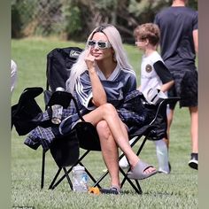 a woman sitting in a folding chair on top of a field next to other people