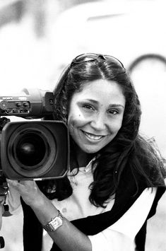 black and white photograph of a woman holding up a video camera in front of her face