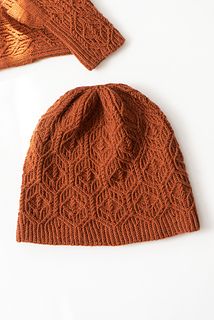 an orange knitted hat and scarf laying on top of a white surface with the same pattern