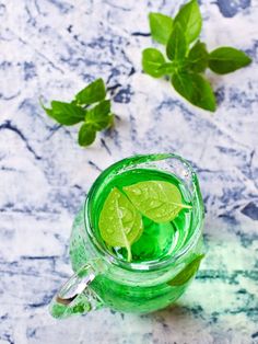 a glass mug filled with green liquid and mint leaves on a marble counter top next to the cup