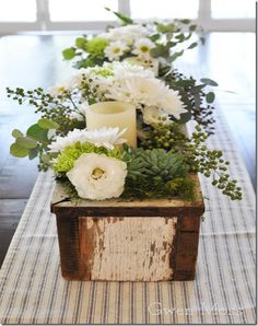 a wooden box with flowers and candles on it sitting on top of a striped table runner