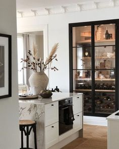 a kitchen with white cabinets and marble counter tops, black framed glass doors on the back wall