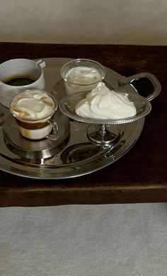 a silver tray topped with two cups of coffee and whipped cream on top of it