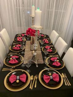 the table is set with black and gold plates, pink napkins, silverware, and candles