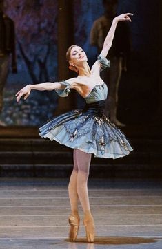 the ballerina is wearing a blue dress and she has her arms outstretched in the air