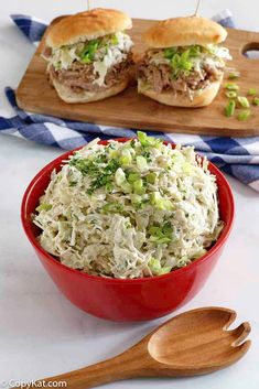 a bowl filled with cole slaw next to two wooden spoons and a cutting board