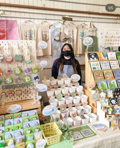 a woman wearing a face mask standing behind a table filled with cupcakes and cakes