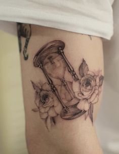 a woman's thigh with an hour and flower tattoo on her leg, which has a clock in the middle