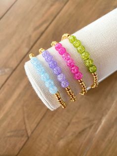 four different colored bracelets sitting on top of a white napkin holder in front of a wooden floor