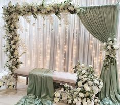 a white and green wedding ceremony setup with flowers on the table, draped drapes