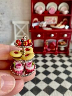 a hand holding a miniature ring with cupcakes on it in front of a red cabinet