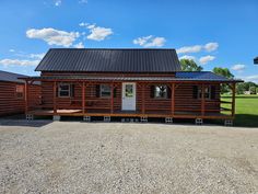 a log cabin sits in the middle of a gravel lot next to a grassy field