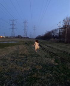 a woman is running through the grass with power lines in the background at night time