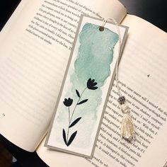 an open book with a watercolor painting on it and a tassel hanging from the cover