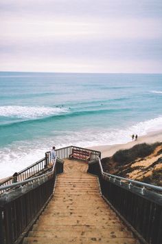 the stairs lead down to the beach where people are swimming in the water and on top of the sand