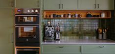 a kitchen with green cabinets and an oven in the middle, next to a coffee maker