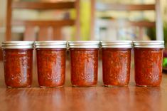 five jars of red sauce sitting on top of a wooden table