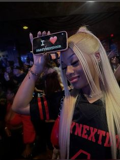 a woman with long blonde hair holding up a cell phone