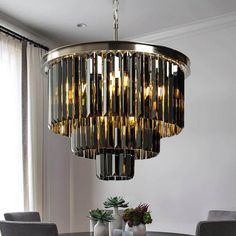 a modern chandelier hangs over a dining room table with grey chairs and potted plants