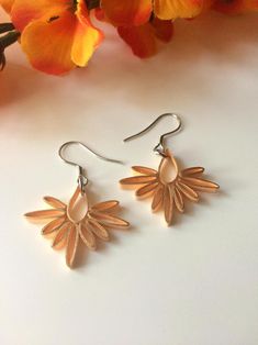 a pair of gold earrings sitting on top of a white table next to orange flowers