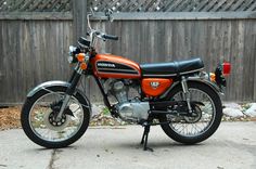 an orange and black motorcycle parked in front of a fence