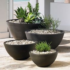 four planters with plants in them sitting on the ground next to a door way