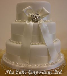 a three tiered wedding cake with white ribbons and pearls on the bottom, adorned with a brooch