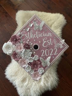 a pink and white graduation cap with flowers on it sitting on top of a furry rug