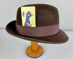 "You'll need this snazzy 1950's fedora to complete your look and turn your suit into an outfit! This fur felt fedora is chocolate brown with a cedar brown grosgrain ribbon band. It has a leather hat band and is fully lined. Made by \"Biltmore\" and sold by \"The Hat Guys\" in Oakland California. This hat is in great vintage condition with no holes, stains, or odors to note. Marked Size: 7 Inner circumference: 22\" Length (at longest point): 11.5\" Width (at widest point): 10.5\" Crown Height: 4\ Brown Fitted Fedora For Kentucky Derby, Fitted Fedora With Short Brim For Derby, Retro Fitted Fedora With Curved Brim, Fitted Retro Fedora With Curved Brim, Retro Fedora With Curved Brim, Vintage Fedora With Wide Brim, Retro Fitted Brimmed Fedora, Vintage Fitted Fedora With Flat Brim, Retro Fedora With Short Brim For Formal Events